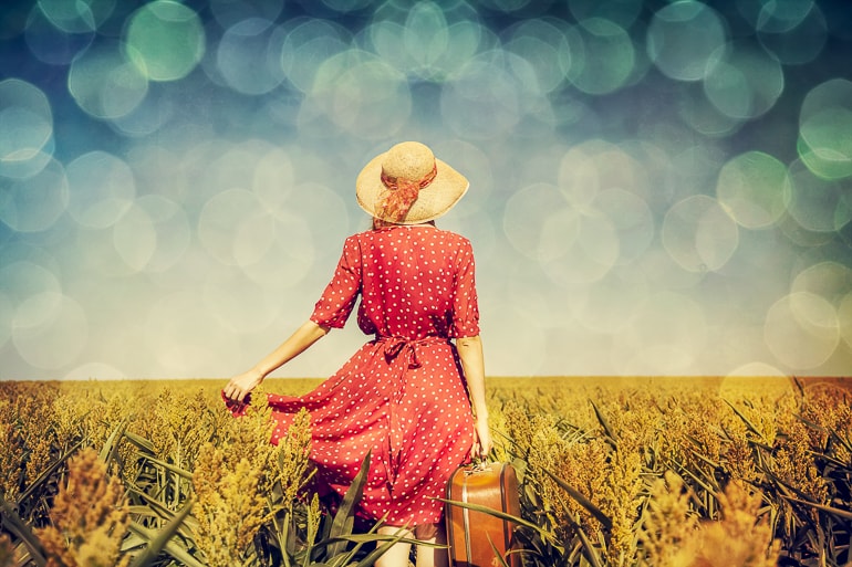 Woman with dress hat and suitcase walking in field captions for girls