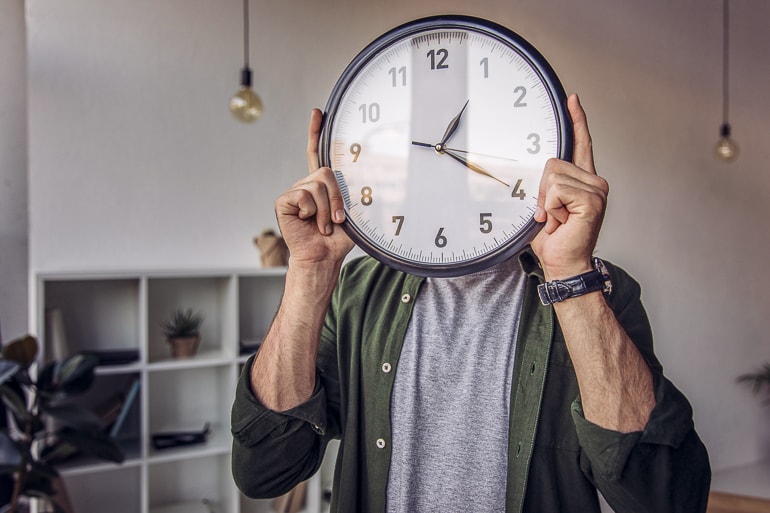 man holding clock in front of face