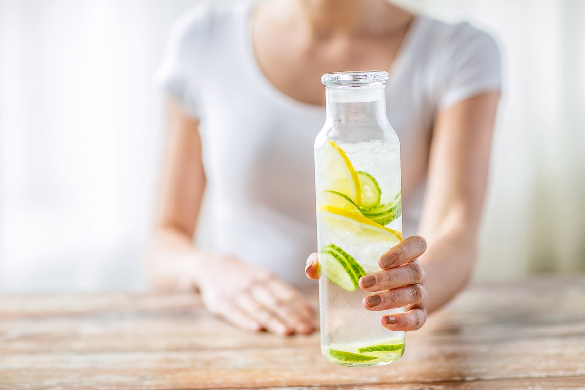Woman holding water bottle with cucumber slices tips to drink more water