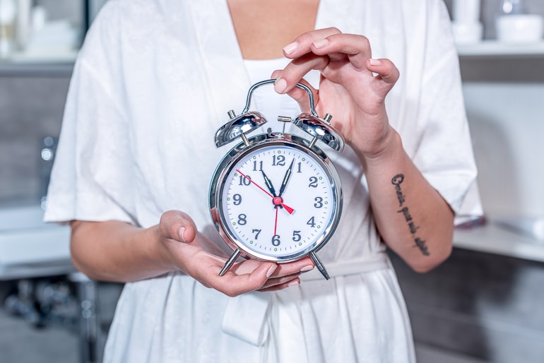 Woman holding a big alarm clock in hand tips to drink water