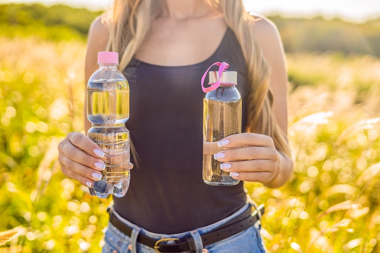Woman holding two water bottles in hand with blurry field in background