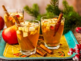 two mugs of apple cider with cinnamon sticks on tray of fall drinks