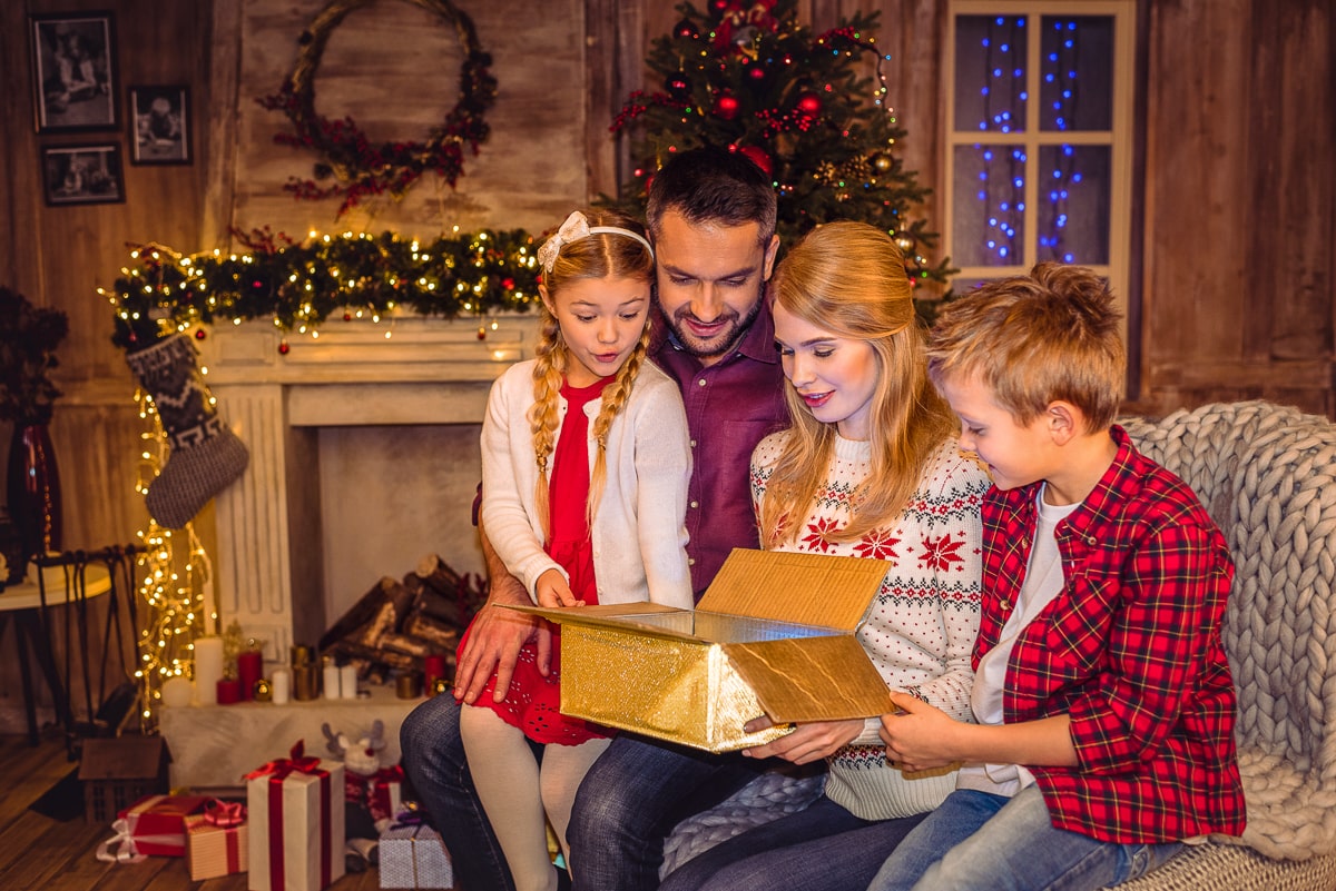 Man woman and two kids sitting in festive living room looking at a present gifts for a mom for christmas