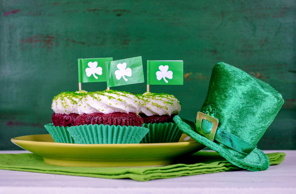 dark cupcakes with icing and green irish flags in top beside green hat st patricks day party