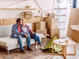 Couple sitting on couch with moving boxes around them things to discuss before moving in together