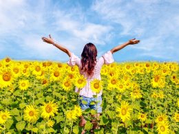 Woman standing in sunflower field with arms stretched out and blue sky in background