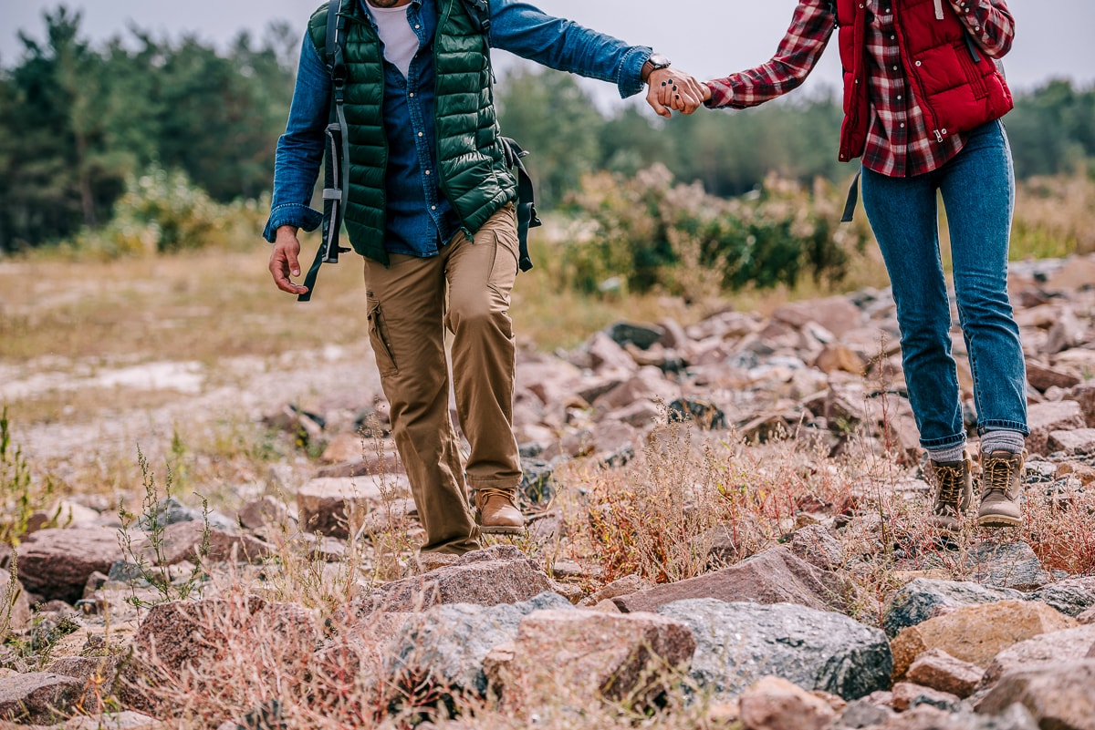 Man and woman with hiking boots and vests walking over rocks on ground benefits of hiking