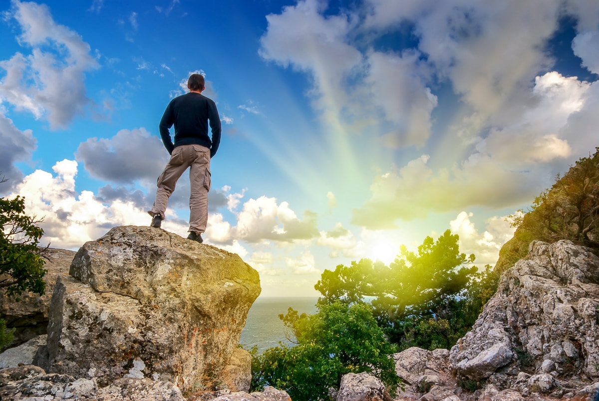 Man standing on rock looking at water blue sky and sun instagram captions for boys