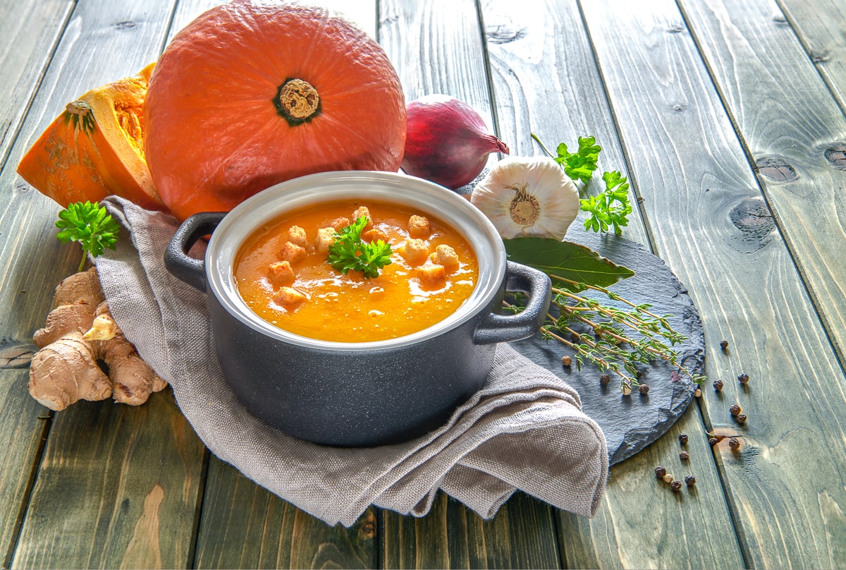 pot of pumpkin soup with dishtowel underneath and orange pumpkin in background.