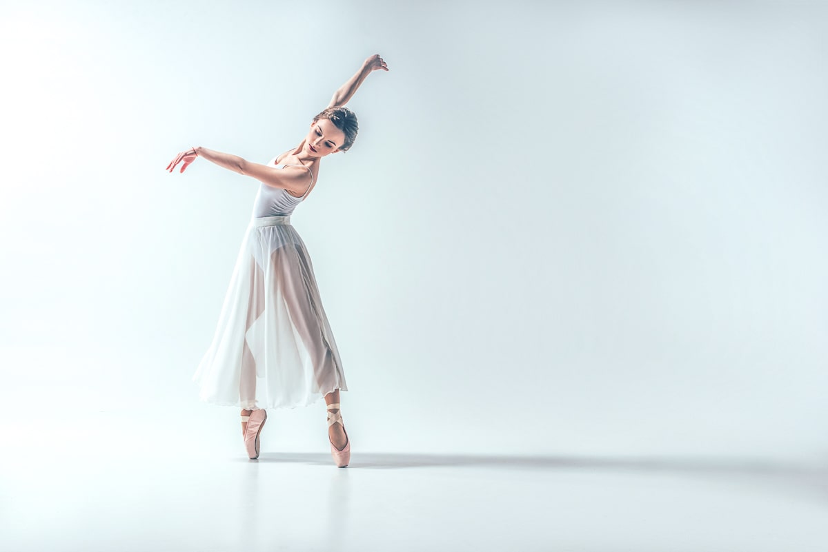 ballerina girl in white dress dancing with white background behind