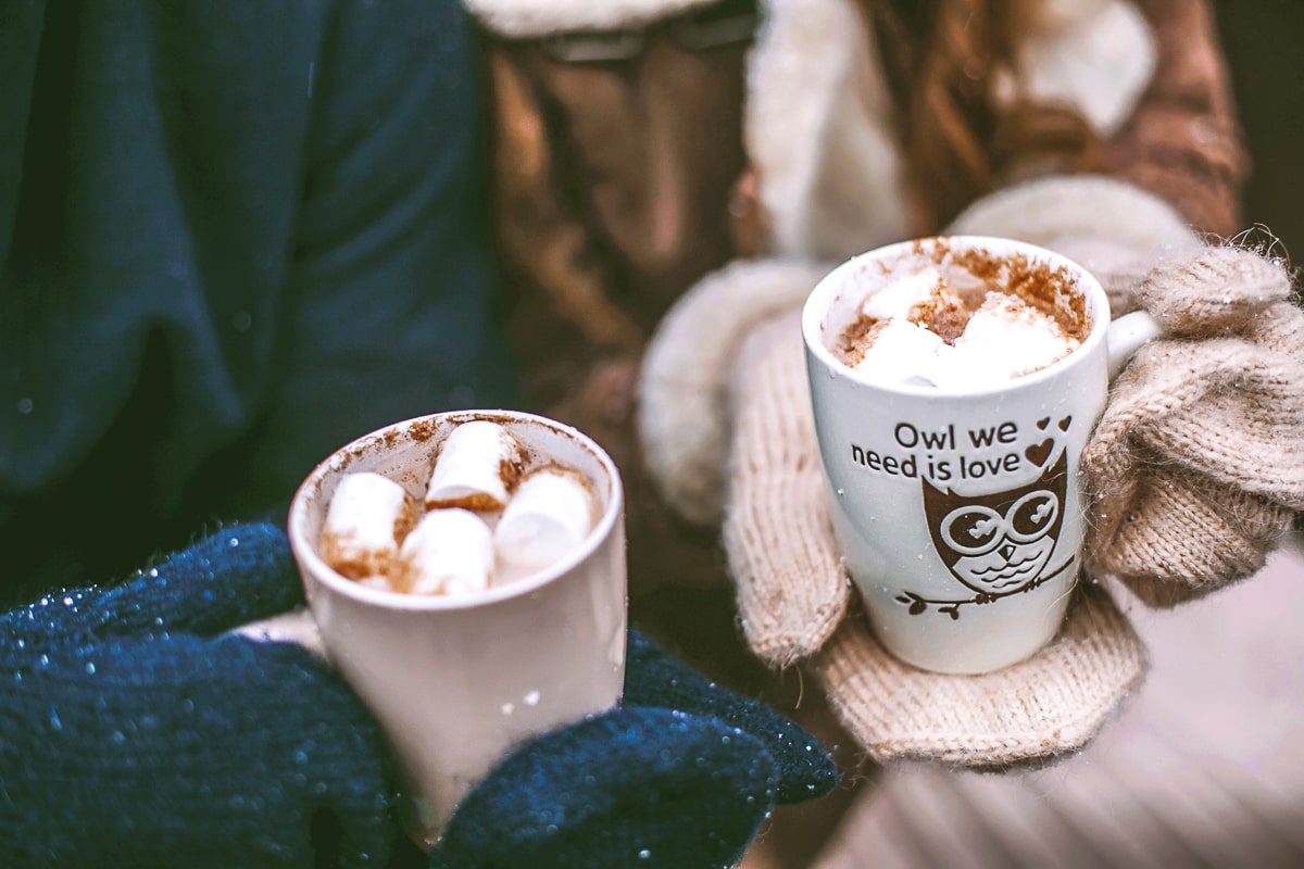 two mugs of hot chocolate held in gloved hands during christmas date