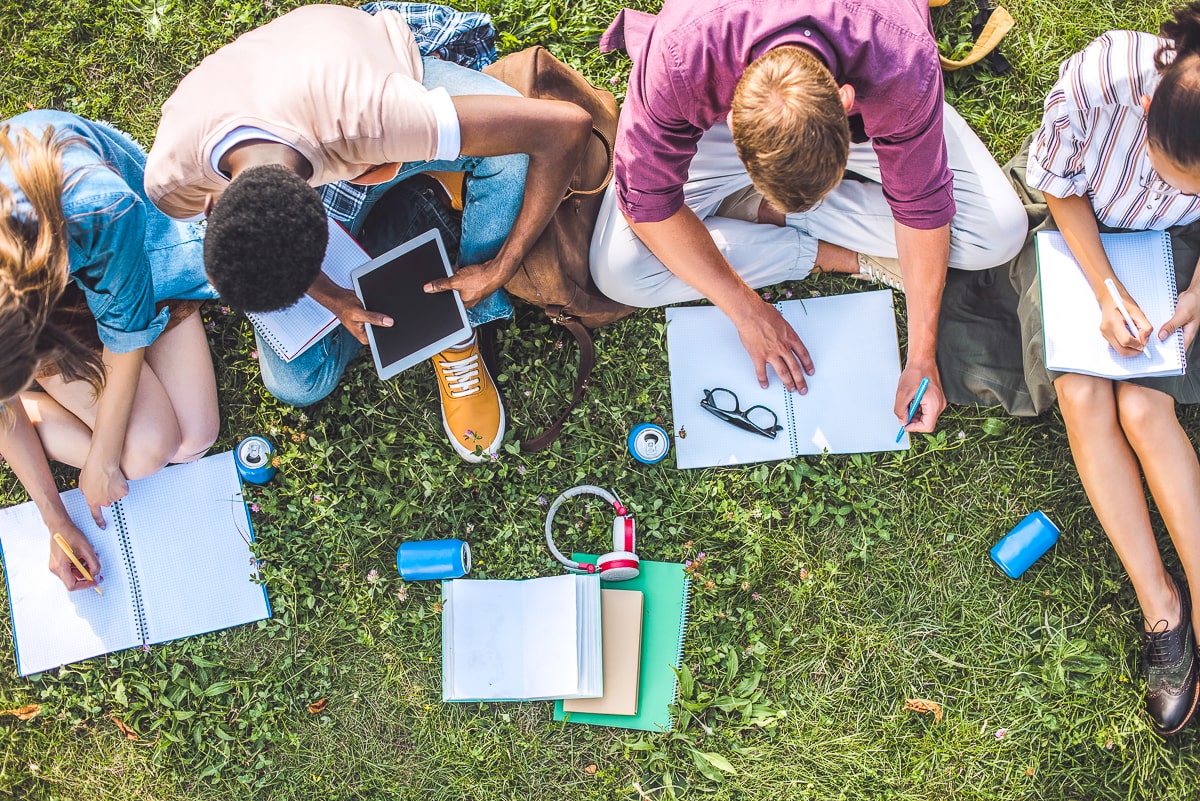 group of college kids sitting on grass with gifts and books around